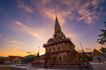 Naklejka premium A stunning view of a traditional Thai temple Wat Chalong with intricate golden architecture, captured during sunset with dramatic clouds and warm sunlight creating a serene and spiritual atmosphere