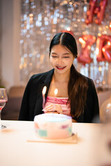 Asian people friends having celebration birthday party together at home with food and drink. Woman excited with birthday cake make a wish and blowing birthday candle with happiness.