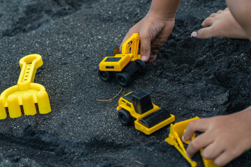 asian boy playing outside with toy cars at the beach. Child, little boy have fun with toy excavator and dumper in the sand