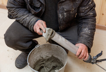 A man is kneeling down and holding a tube of cement