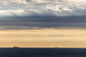 Two ships on the horizon under a dramatic sky at sunset, showcasing tranquility and vastness of the sea.