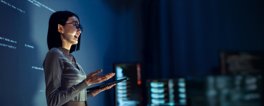 asian woman programmer standing in front of a screen with code projected  presentation the integration of technology and human expertise in software development
