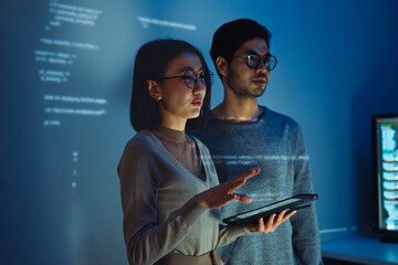 Asian Two software developers engaged in collaborative coding session, with code projected onto the...