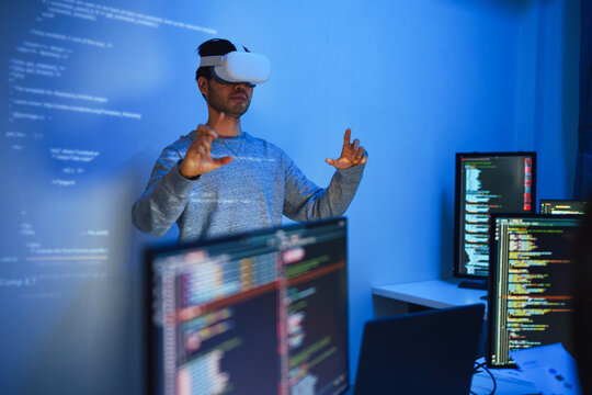 developer uses a VR headset to interact with projected interface designs, while colleagues discuss and code on screens, highlighting the integration of virtual reality and UI/UX design 