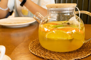 Fruit tea in a glass teapot made of oranges and apples on the table.