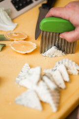 A green handled crinkle cutter slices soft blue cheese on a yellow cutting board, with citrus slices and a knife visible in the background.