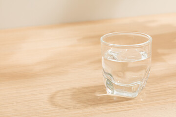 Glass of water isolated on wooden background. Warm lighting background. Wooden surface. Light and Shadow wallpaper. Space for text. Backdrop. Studio photography. Still life. 