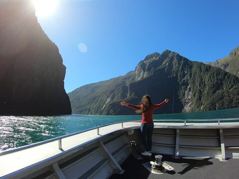 A female standing on the Cruise ship sailing through The Sounds, Mitre Peak and waterfalls at Milford Sound, Fiordland National Park. New Zealand tourist attraction. 