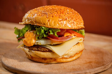 Photo of burger with sesame seed bun, salad, cheese and bacon on a round wooden tray on the table of a wooden bar or restaurant next to a brick wall prepared for snack time