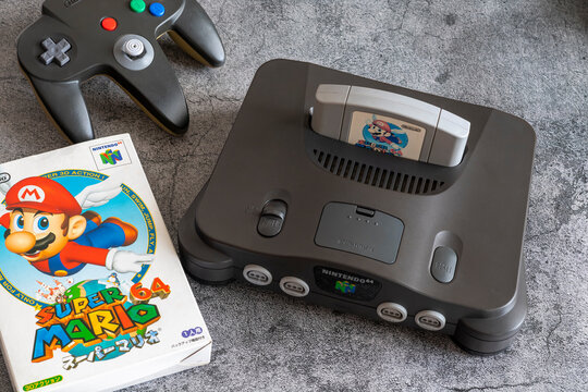 Fukuoka, Japan - january 3, 2025 : the famous nintendo 1996's hit Super Mario 64 game plugged in the original nintendo N64 video game console and controller on a concrete ground