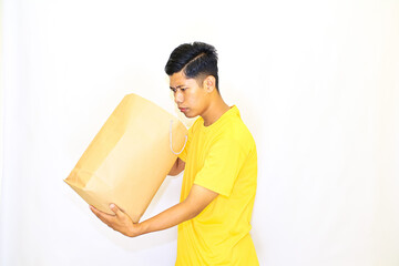 Obraz premium Adult Asian man in yellow t-shirt holding tote bag on white background, man doing shopping