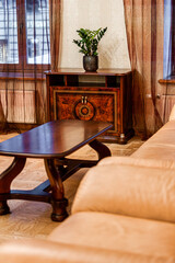 Indoor setting featuring a polished wooden coffee table, beige leather sofa, vintage style cabinet with inlay work, and sheer brown curtains.