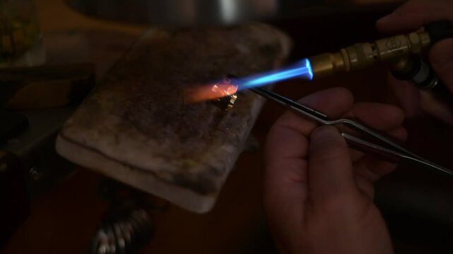 Professional jeweler refining golden ring, welding blowtorch and tweezers during meticulous metalworking process, showcasing precision craftsmanship with detail. Experienced goldsmith