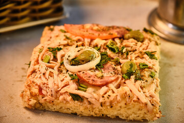 Photo of savory focaccia pie on a wooden bar or restaurant table with a paper base and surrounded by a can of soda and a jar of sugar and a basket of condiments prepared for breakfast or afternoon