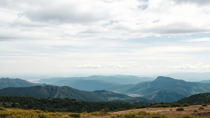 Naklejka premium Serene Vista of Rolling Hills and Distant Mountains Under a Cloudy Sky
