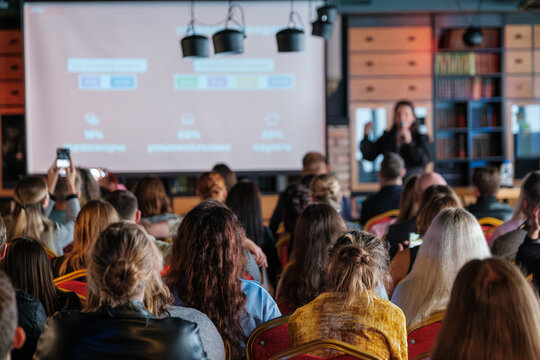 Large audience attending a speaker's presentation in a conference room focused on business ideas and networking. The event includes impactful visuals on the screen to convey messages.