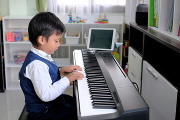 Asian little kid learning piano online at home with digital tablet.