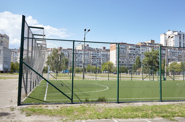Lawn field for playing football behind the green fence mesh at school territory. Close-up of soccer field with green grass
