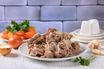 pork and beef bones with leftover meat after cooking broth on a white plate with carrot, onion and...