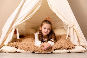 Happy 6-7 years old smiling little blonde girl in white dress lying in a wigwam tent in children room at home. Childhood, games, imagination. High quality photo © Irina Mikhailichenko