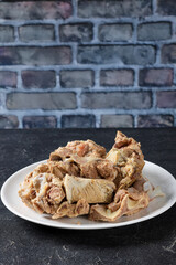 pork and beef bones with leftover meat after cooking broth on a white plate on concrete table with brick wall at background, close-up, vertical view