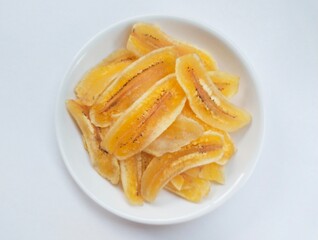 Close-up of banana chips in plate on white background.