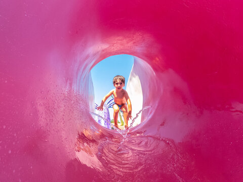 Child sliding down pink waterslide at water park, summer vacation fun
