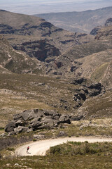 A cyclist descending a steep gravel road down a mountain pass leading to a deep valley.