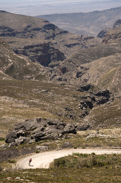 A cyclist descending a steep gravel road down a mountain pass leading to a deep valley.