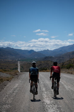 Two friends cycling down a long gravel road in the wilderness during a bicycle riding adventure in vast open spaces.