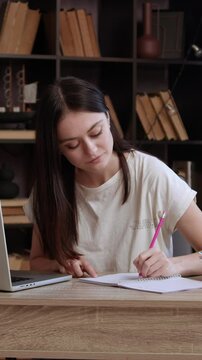 Young woman student makes notes while looking at laptop