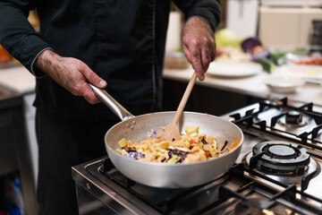 Close up of professional chef mixing vegetarian meal ingredients with ladle in cooking pan.