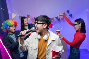 Group of Asian male and female friends They are having fun and dancing together. Sing karaoke at a house party drink cocktails together A room lit up with disco neon lights. New Year's Eve party idea