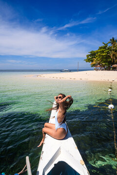 Young asian woman sitting on boat prow, Guyam island, Siargao