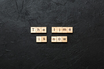 the time is now word written on wood block. the time is now text on table, concept
