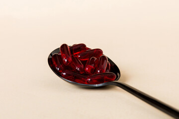 Vitamin capsules in a spoon on a colored background. Pills served as a healthy meal. Red soft gel vitamin supplement capsules on spoon
