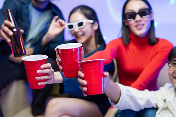 Close-up shot, focus on glasses. Group of happy Asian friends having fun, smiling at a party, clinking glasses. A young man and woman have fun at a colorful party at home. By wearing dark sunglasses