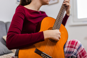 Fototapeta premium Young woman strumming her guitar in the comfort of her room.