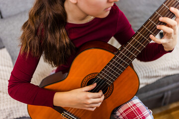 Young woman strumming her guitar in the comfort of her room.
