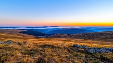 Obraz premium Vast mountainous landscape at sunset with rolling clouds and golden grass.
