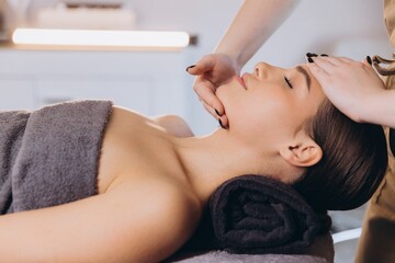 Masseuse performing relaxing face massage therapy on young woman