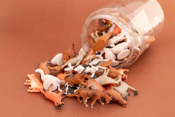 Miniature plastic toy animals spilled out from a transparent container on a brown background