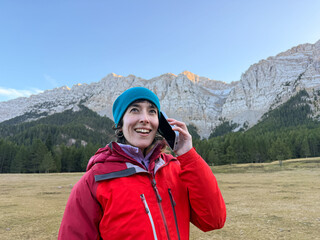 A woman in a red jacket and blue hat is talking on her cell phone