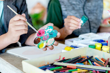 Learning to use poster color to draw various pictures of asian boys on a table outside classroom...
