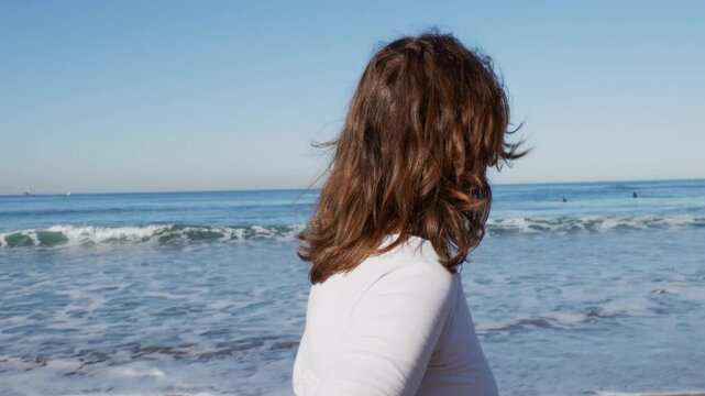 Mujer disfrutando al caminar por la orilla de la playa, mira hacia el mar, surfista de fondo plano corto