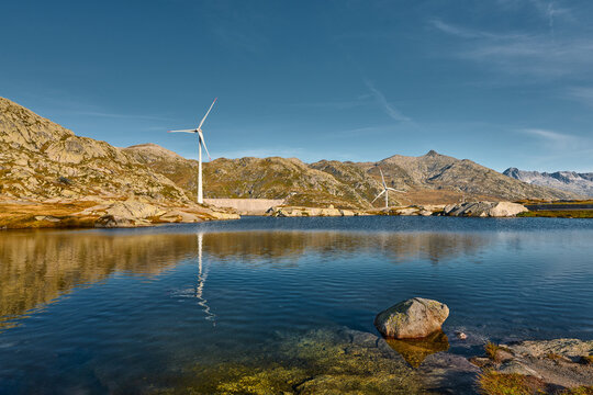 Malerische Szene einer im Bergsee spiegelnden Windturbine, des Windparks auf dem kargen Gotthardpass in den Schweizer Alpen
