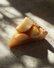 Slice of pear tart with glistening glaze on a textured surface, casting soft shadows.