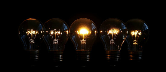 A row of light bulbs, one glowing brightly in the middle against a black background, symbolizing ideas and innovation.