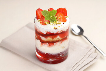 Tasty trifle dessert. Strawberries, sponge cake and whipped cream in glass on beige table