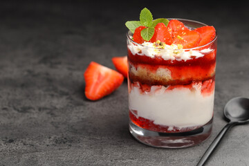 Tasty trifle dessert. Strawberries, sponge cake and whipped cream in glass on grey table, space for text